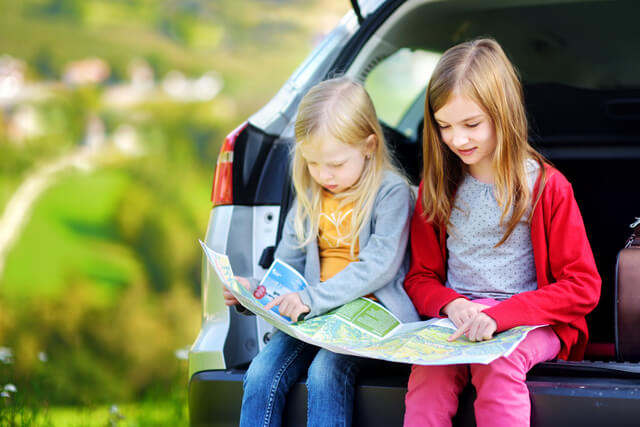 two little girls reading a map sat on the boot of a car