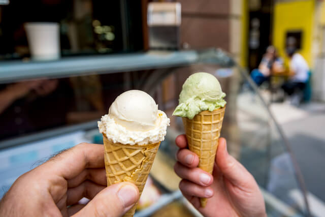 Two hands holding ice cream in a waffle cone