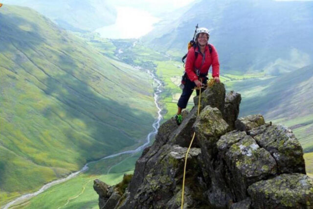 A woman attached with rope climbing on a rocky outcrop