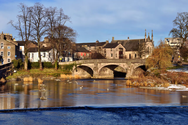 A view across the River Kent towards a bridge and houses in Kendal