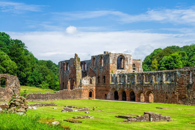 The ruins of Furness Abbey sat on a green lawn with a blue sky above