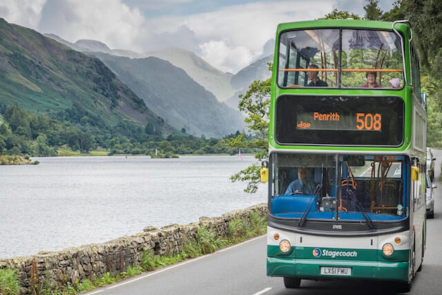 A bus driving on the main road with a lake on the left hand side