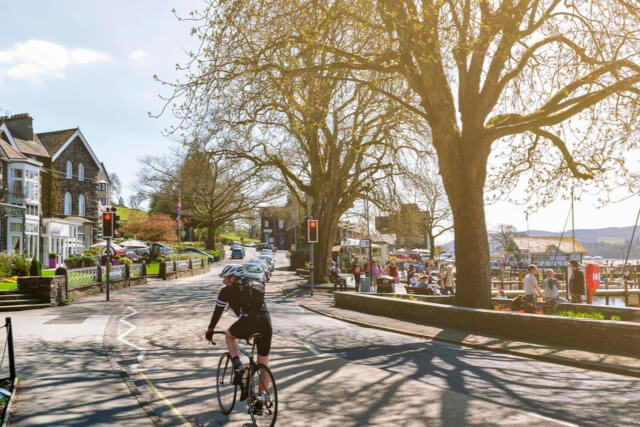 A cyclist riding a bike on a main road with a lake on the right hand side