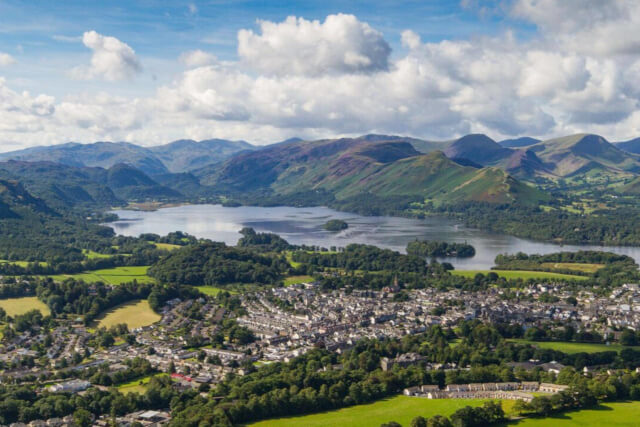 A view across the rooftops of a town from a position on a hill with a lake and mountains in the distance