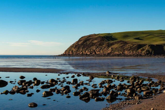 A view across the shore from the Cumbria coastline with rocks and water on the beach