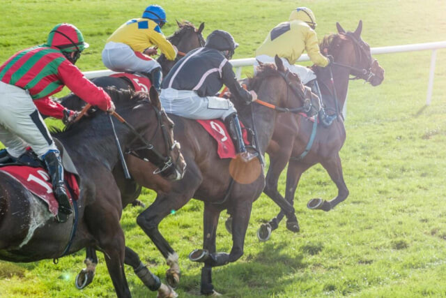 Men riding horses around a racecourse track