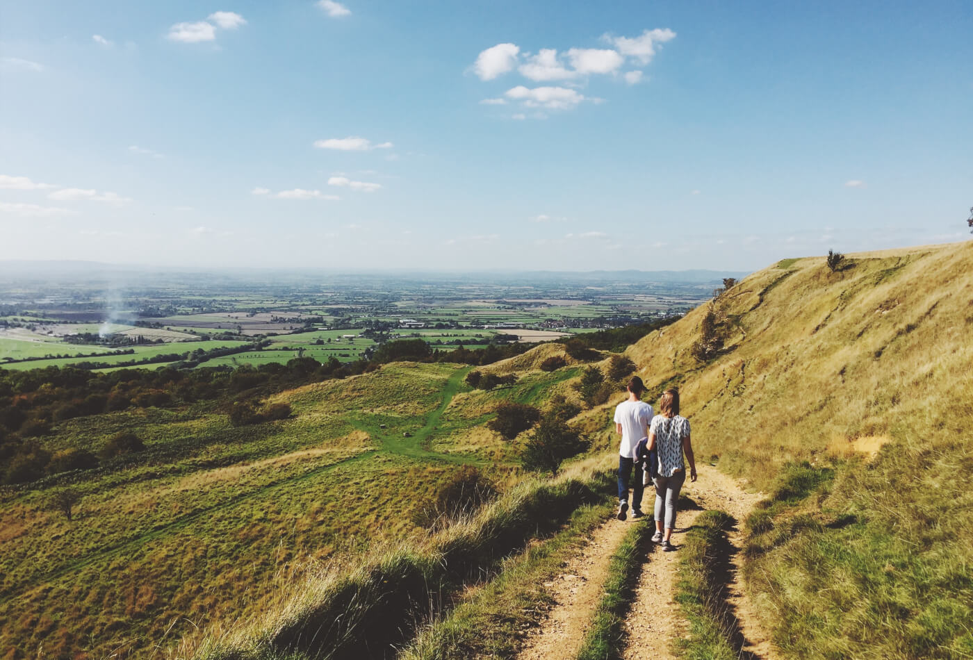 Two people walking along a countryside path surrounded by greenery