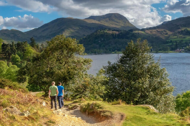 Two people walking on a countryside path with a lake and mountains in the distance