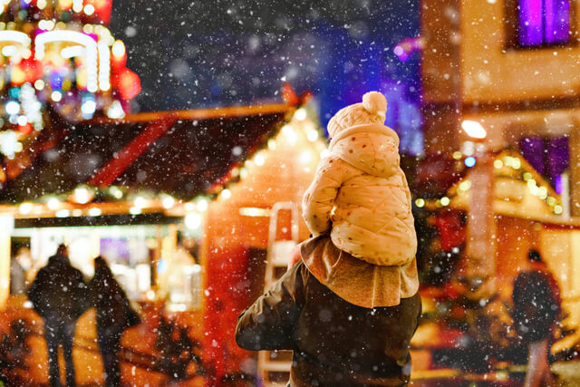 A father with his daughter sat on his shoulders at a christmas market