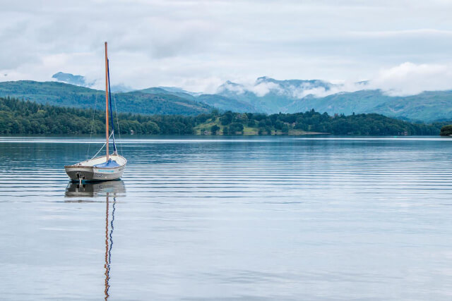 A small boat floating on Lake Windermere with cloudy fells in the background
