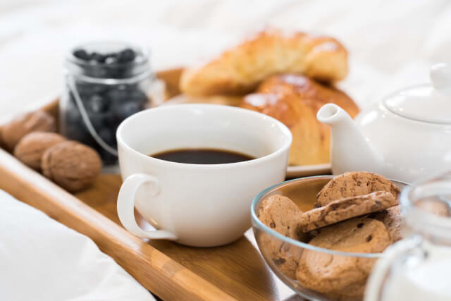 A wooden tray carrying a cup of coffee abowl of biscuits and some croissants