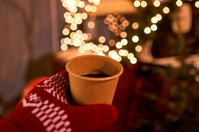 a gloved hand holding a mug of mulled wine at a christmas market