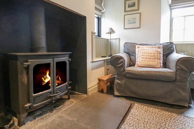 A grey sofa sat in front of a woodburning stove in a cosy cottage