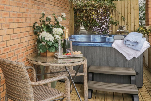 A small table with two chairs holding a tray of champagne and fruit with a hot tub in the background