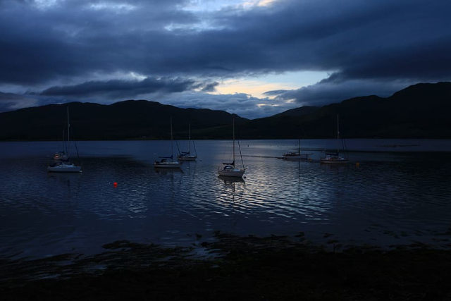 A view across a gloomy lake with boats on the water under a dark sky