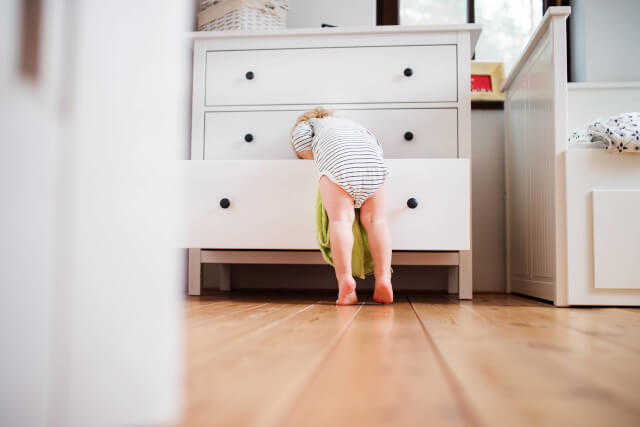 A young child wearing a striped babygrow leaning into the drawer of a chest