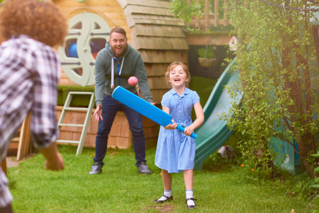 A young girl holding a cricket bat about to hit a ball