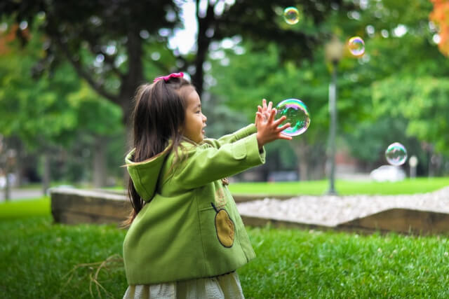 A young girl in a green coat catching a bubble