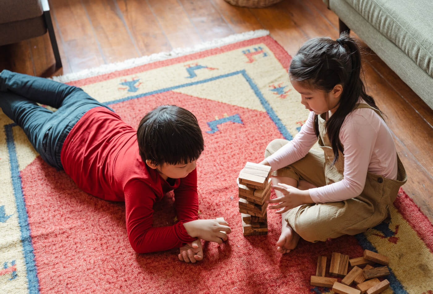 Two young children sat on a rug on the floor playing a game of jenga
