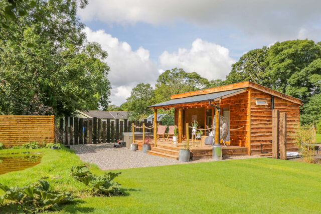 A wooden cabin with a decked area at the front and garden furniture