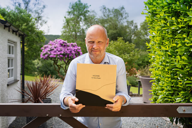 Simon Rogan holding a Home by Simon Rogan brown box in his hands