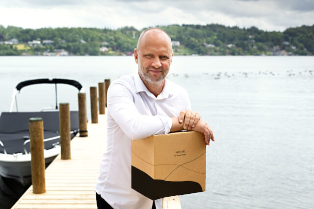 Simon Rogan posing with a Home by Simon Rogan meal box in front of a large lake