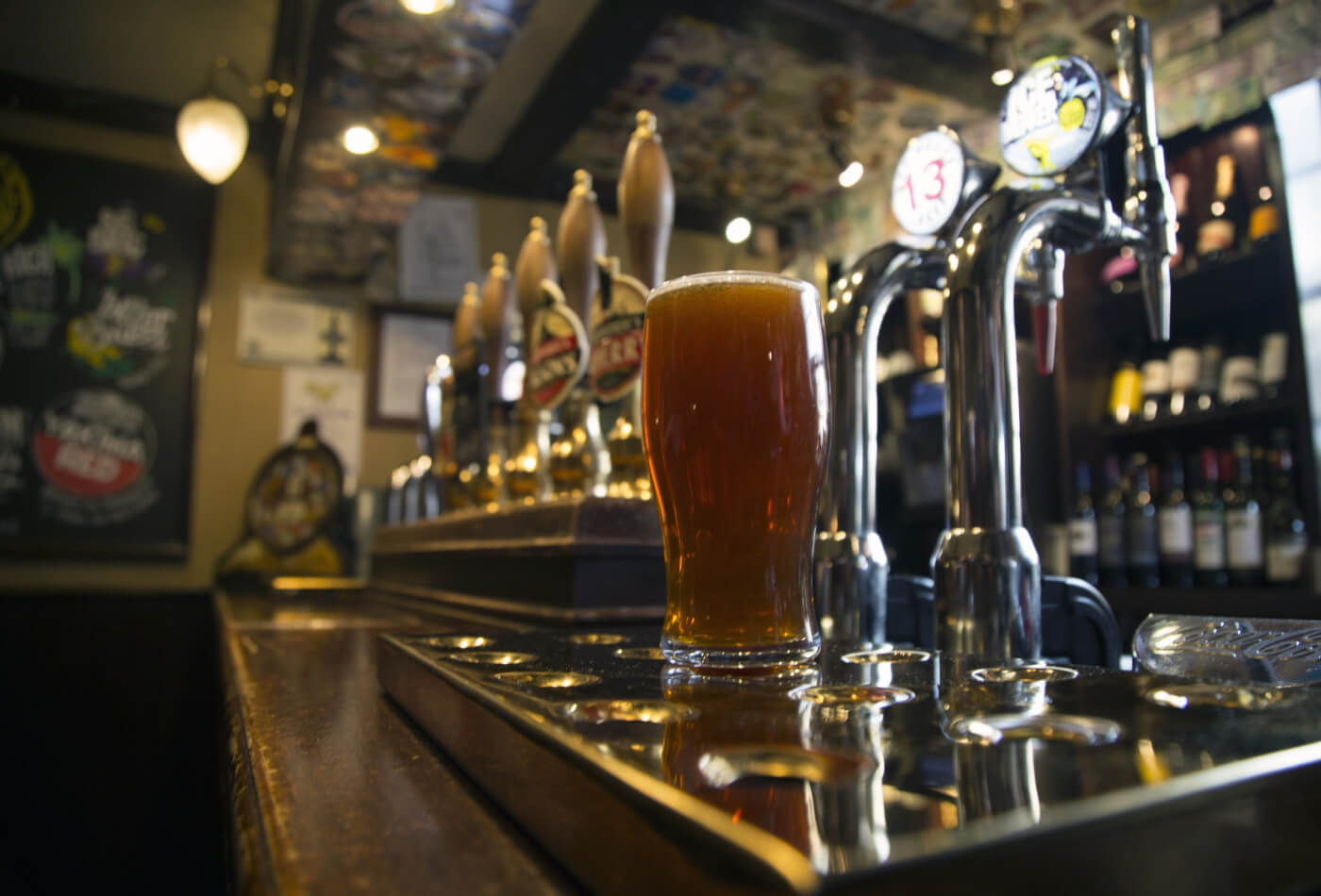 A pint of lager in front of beer taps in a pub