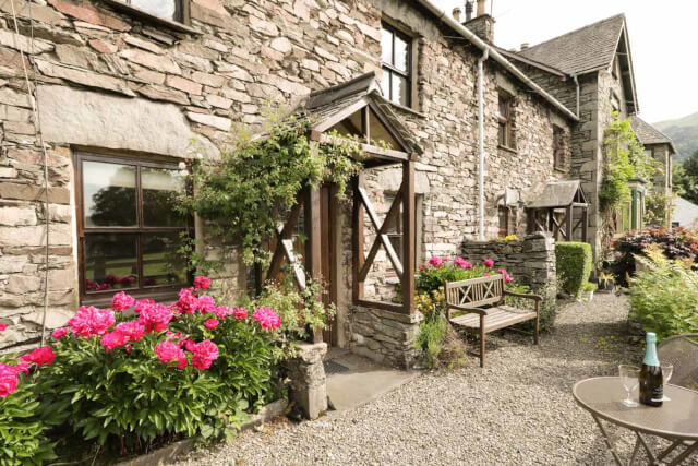 A traditional stonebuilt cottage with flowers and greenery climbing the walls