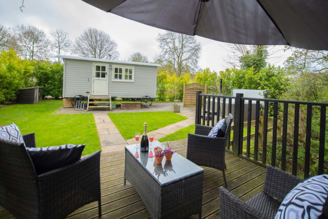 An outdoor seating area with drinks on the table and a shepherds hut in the background