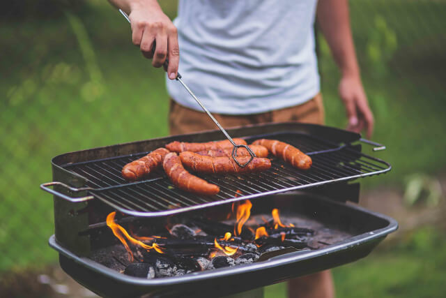 Sausages being cooked on a bbq being poked with a skewer 