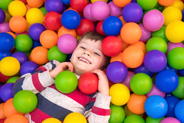 A young boy lying amongst balls at an indoor soft play