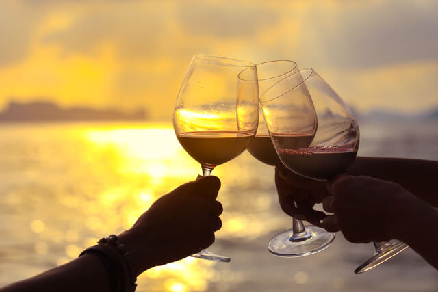 Three hands toasting a glass of red wine by a lake
