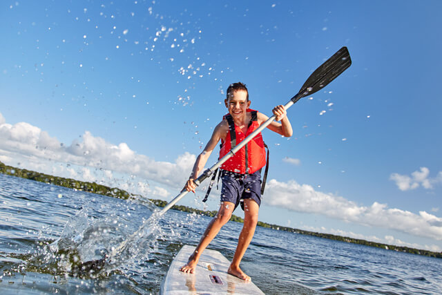A boy standing up on a paddleboard on the water