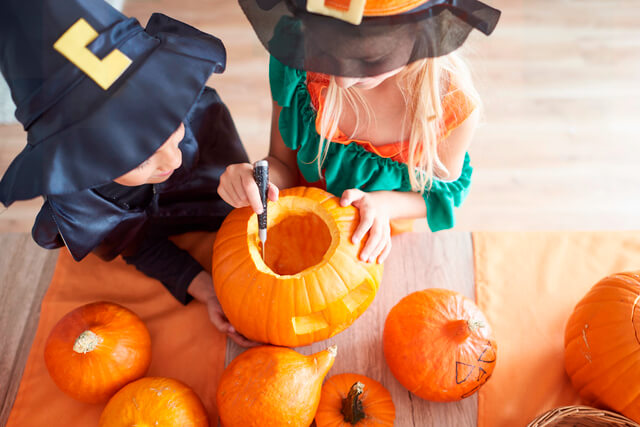 Two young children dressed in witches costumes carving pumpkins