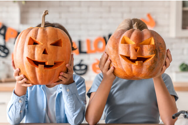 Two young children with carved pumpkins covering their faces