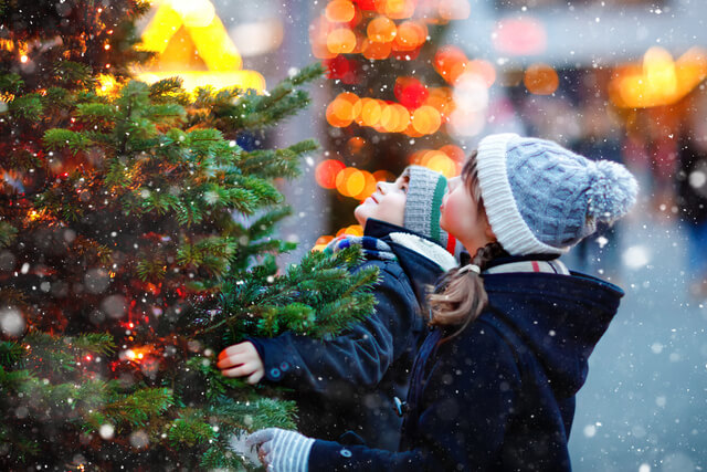 A child and woman stood next to a christmas tree in winter