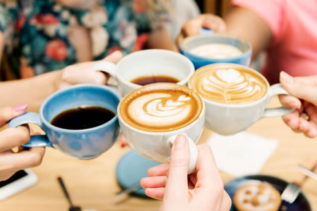 Friends toasting mugs of coffee and tea in a cafe