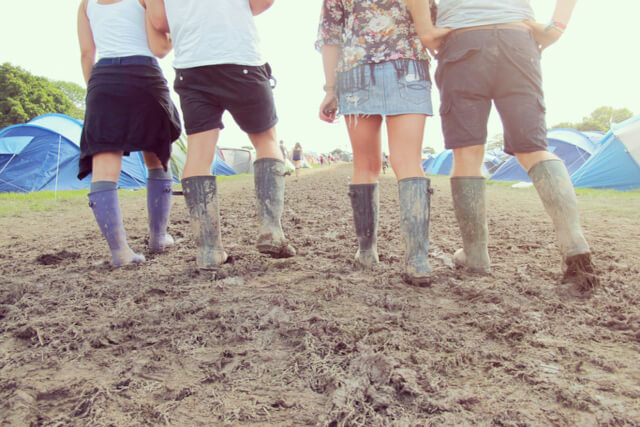 A group of festival goers walking in wellies through a festival campsite