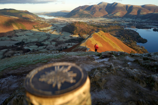 A hiker approaching the summit marker at Catbells in the Lake District 