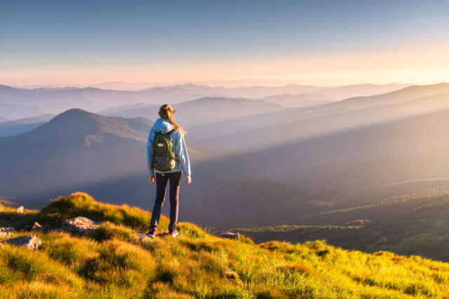 A woman gazing over the surrounding hills from the top of a grassy mountain 