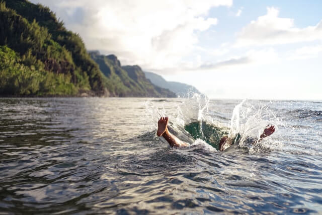 A body jumping into a body of water with grassy mountains in the background