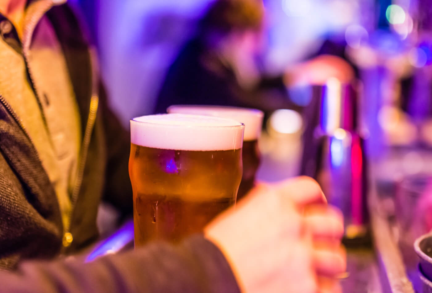 A man standing at the bar with two pints of beer