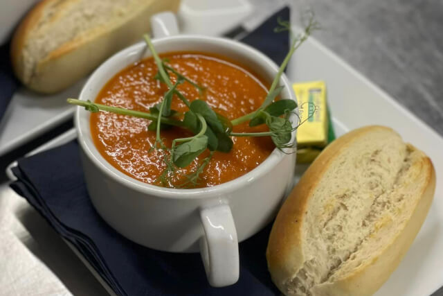 A mug of red soup with a bread roll on a plate