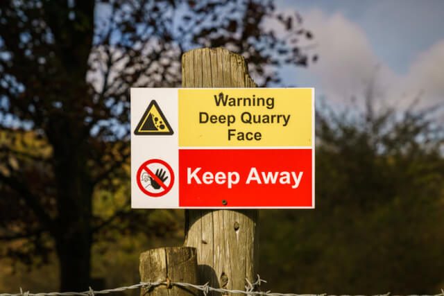 Red and yellow sign warning against the dangers of a deep quarry face