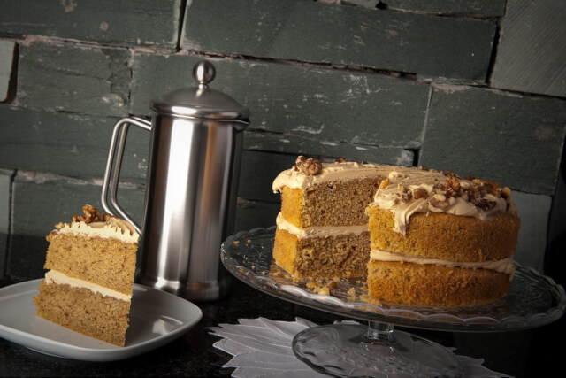 A coffee and walnut cake with a slice missing sitting on a cake stand