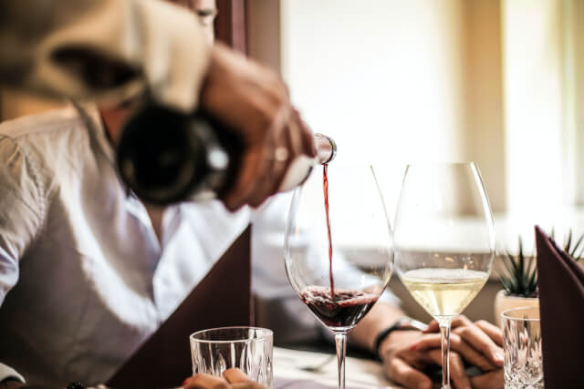 A waiter pouring a bottle of red into a glass at a restaurant
