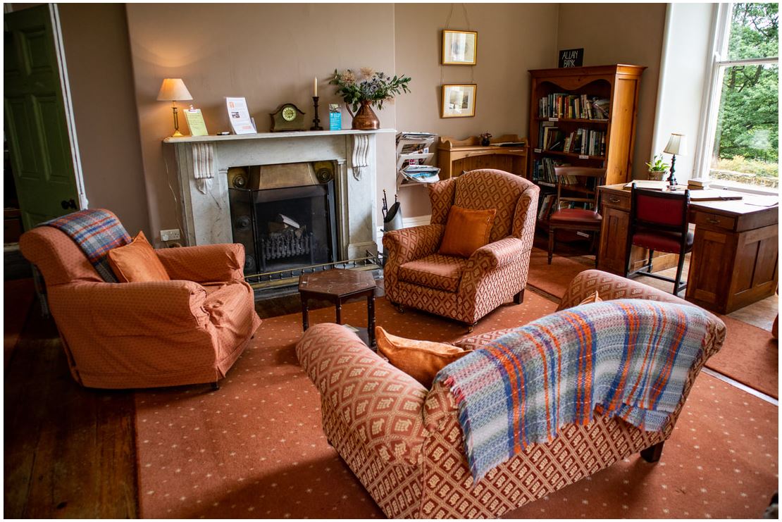 Cosy indoor living area at Allan Bank National Trust House in Grasmere - arm chairs aruond the log fire and bookshelves