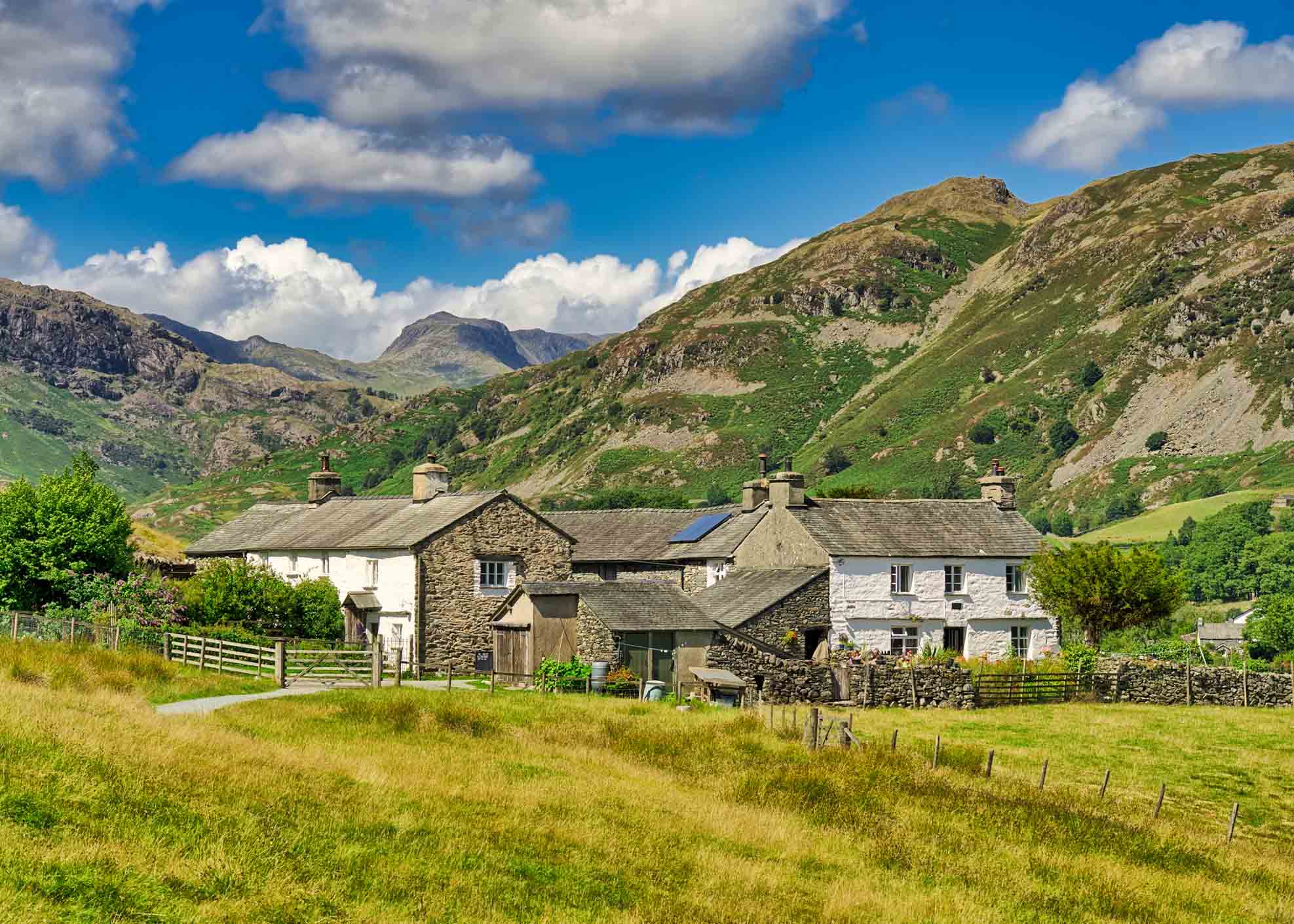 A group of traditional whitwashed cottages in the English Lake District, with Bowfell in the distance.