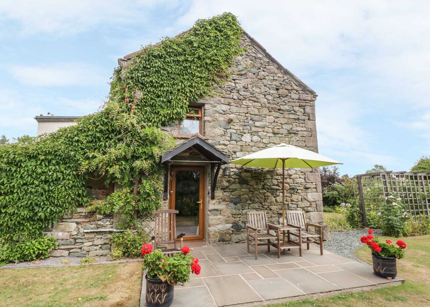 Stone built Lake District Cottage with pretty green plants growing up the walls and flowers in the garden