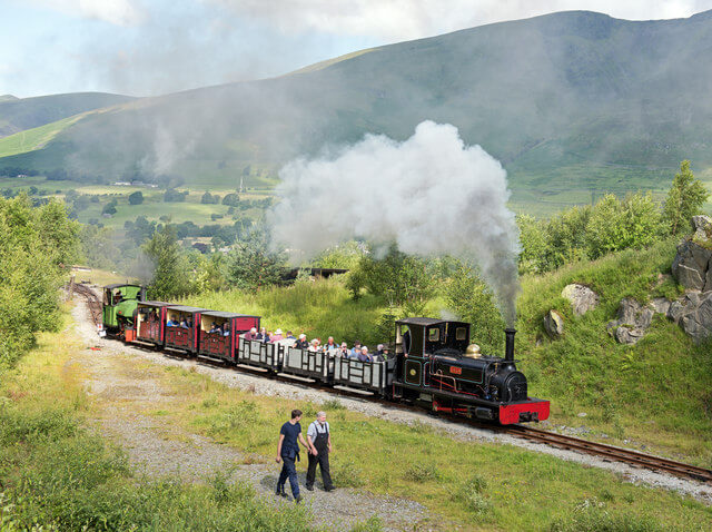 A photograph of a steam train with passengers passing through the Lake District towards Threlkeld Quarry and Mining Museum